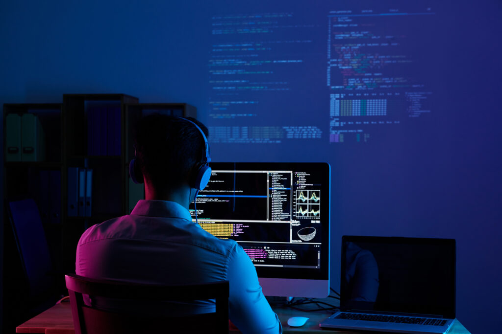 Person coding in dark room with multiple computer screens